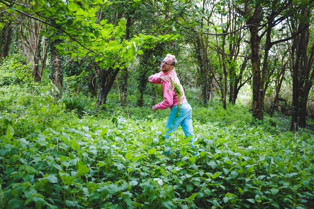 Simon in a forest trying to get some green stuff off his back