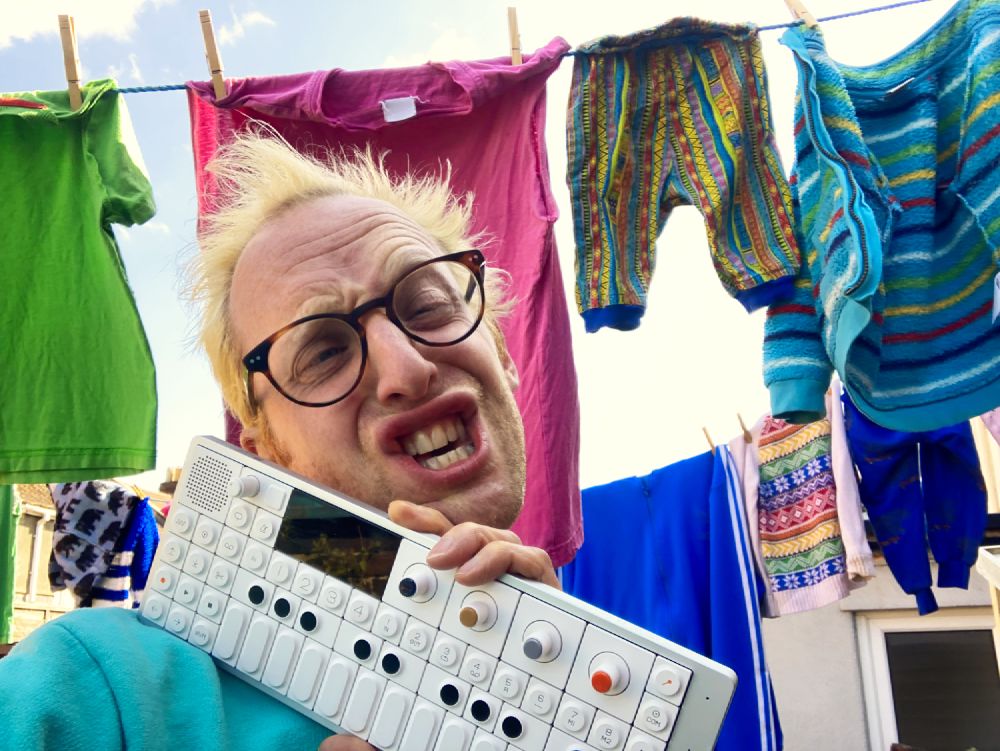 Simon holding his OP-1 pulling a silly face in front of some washing hanging on the line like an absolute champ